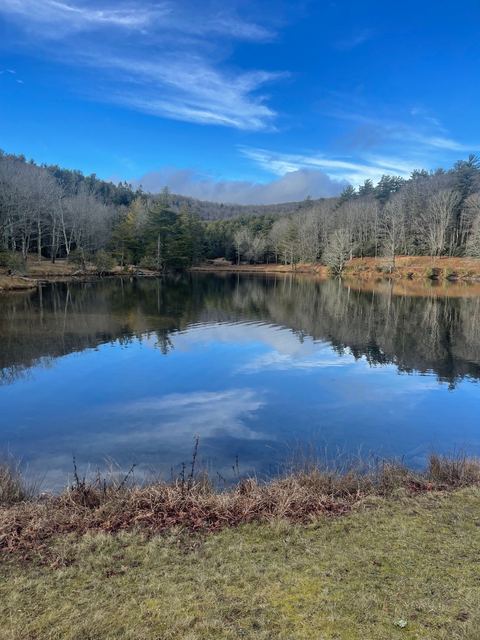 Bass Lake in late fall, perfectly still, reflecting bare trees, evergreens and a deep blue sky